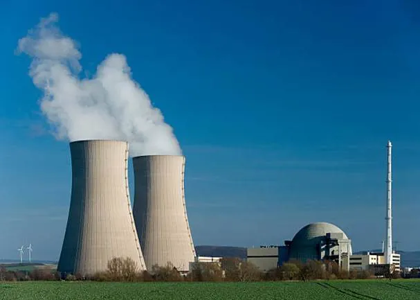 Fotografía de dos torres de refrigeración de tiro natural expulsando vapor junto a la cúpula del reactor de una central nuclear