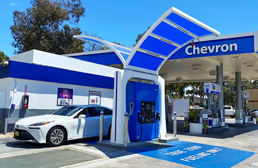 Fotografía de un surtidor de hidrógeno azul en una estación de servicio Chevron, junto a un turismo blanco de pila de combustible